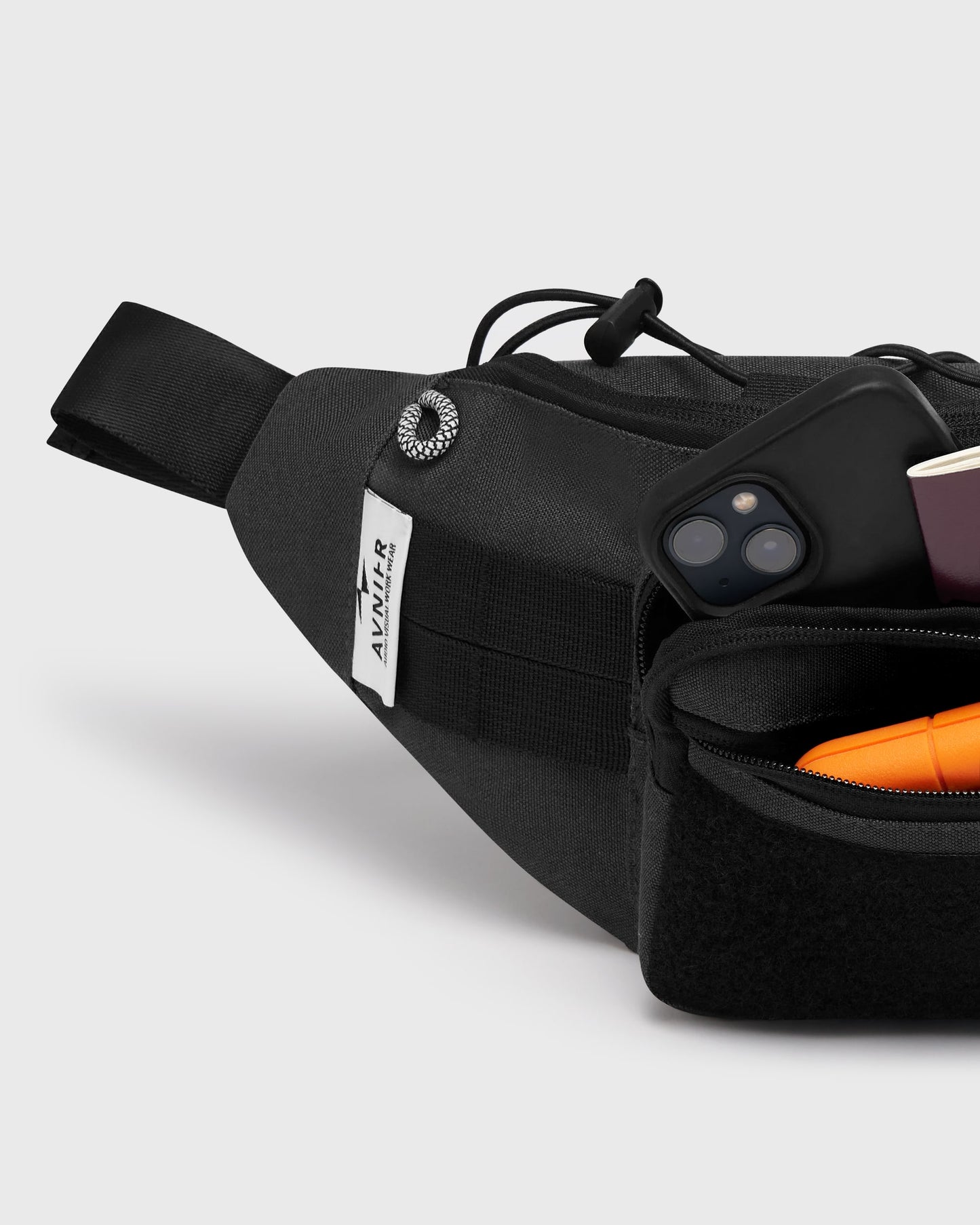 Détail de la banane noire Avnier, poche avant avec accessoires rangés — logo Avnier visible, design technique workwear.