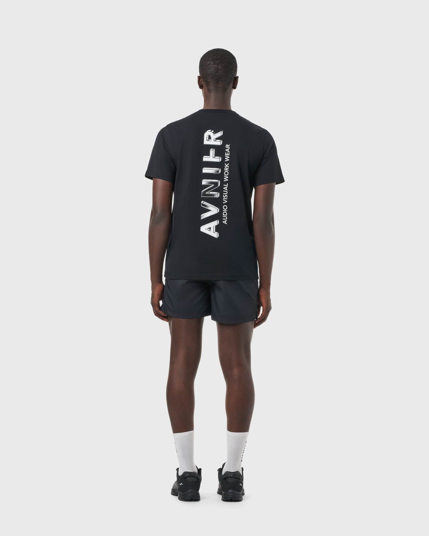 T-shirt noir Avnier Source Black Chrome Vertical porté par un homme, vue de dos, grand logo vertical graphique.