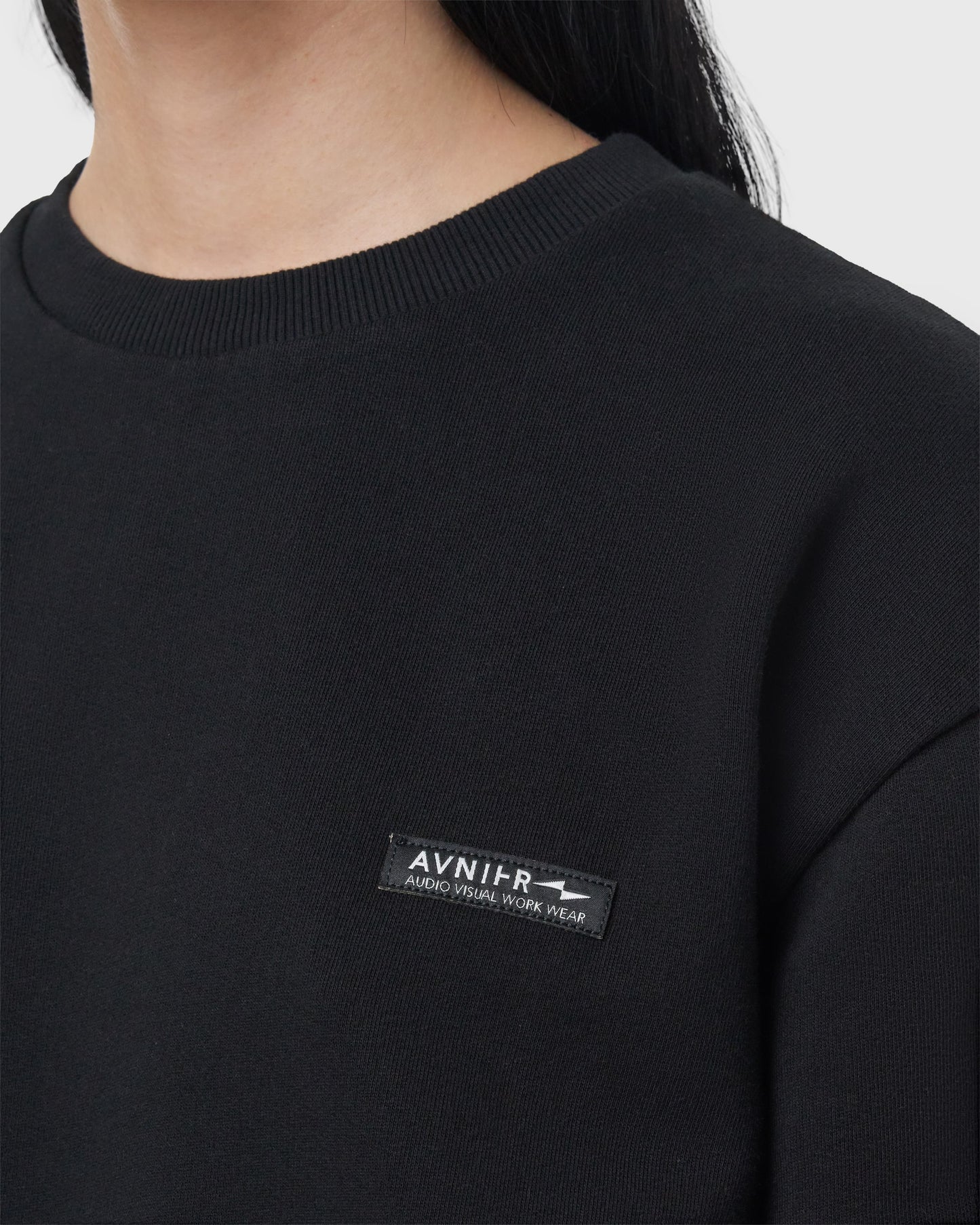 Détail du logo brodé Avnier sur le sweat noir Encore V4, design sobre et premium.