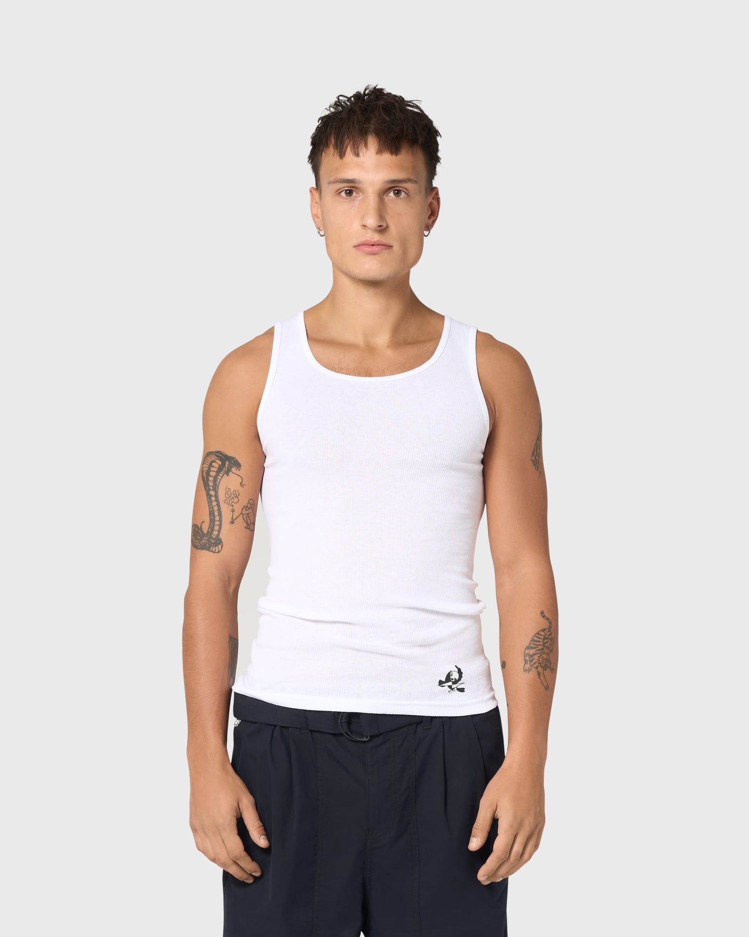 Débardeur blanc AVNIER × TUCO, vue de face sur modèle, coupe ajustée en coton côtelé, logo imprimé sur le bas.