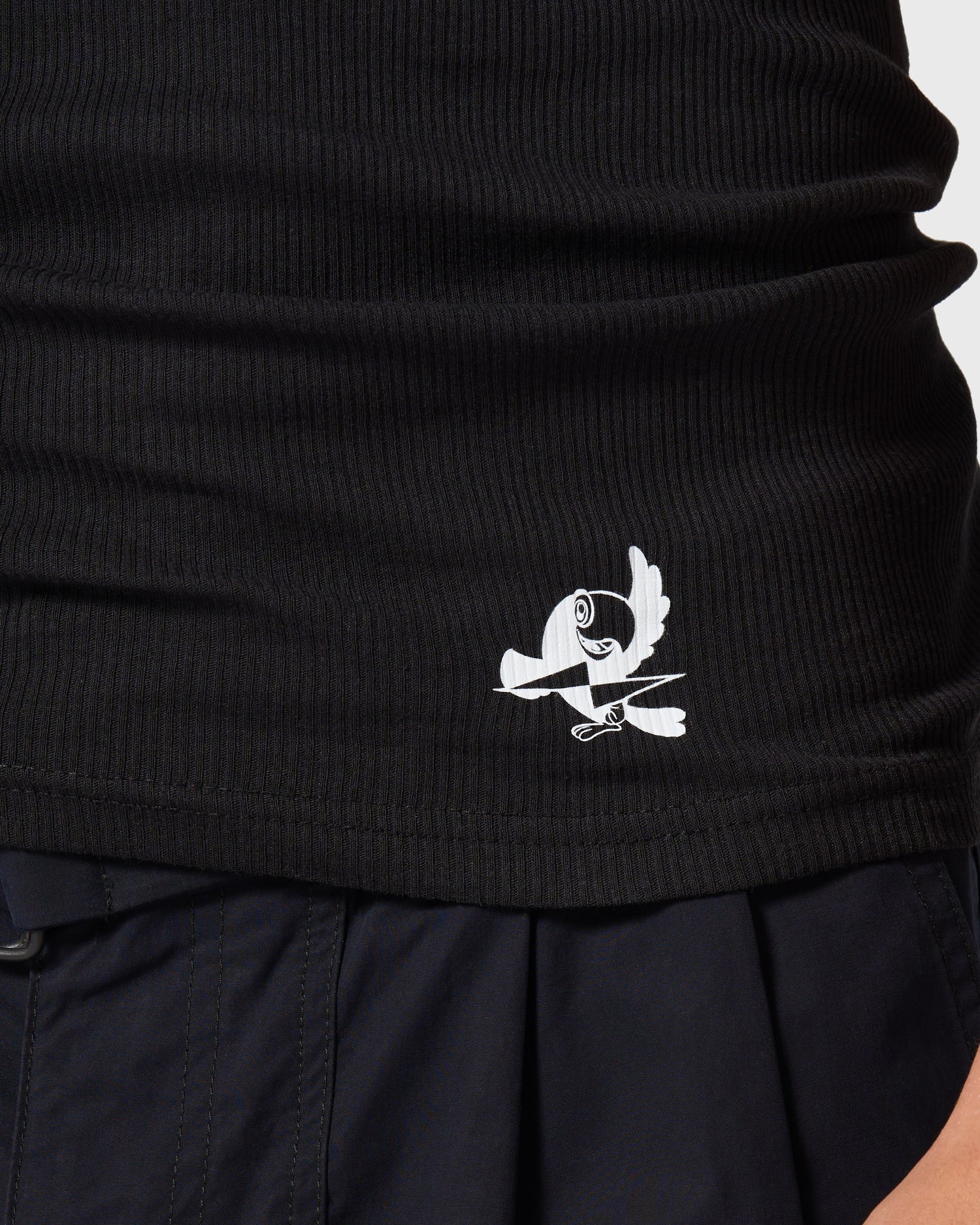 Détail du logo imprimé sur le bas du débardeur noir AVNIER × TUCO, texture côtelée et finition premium.