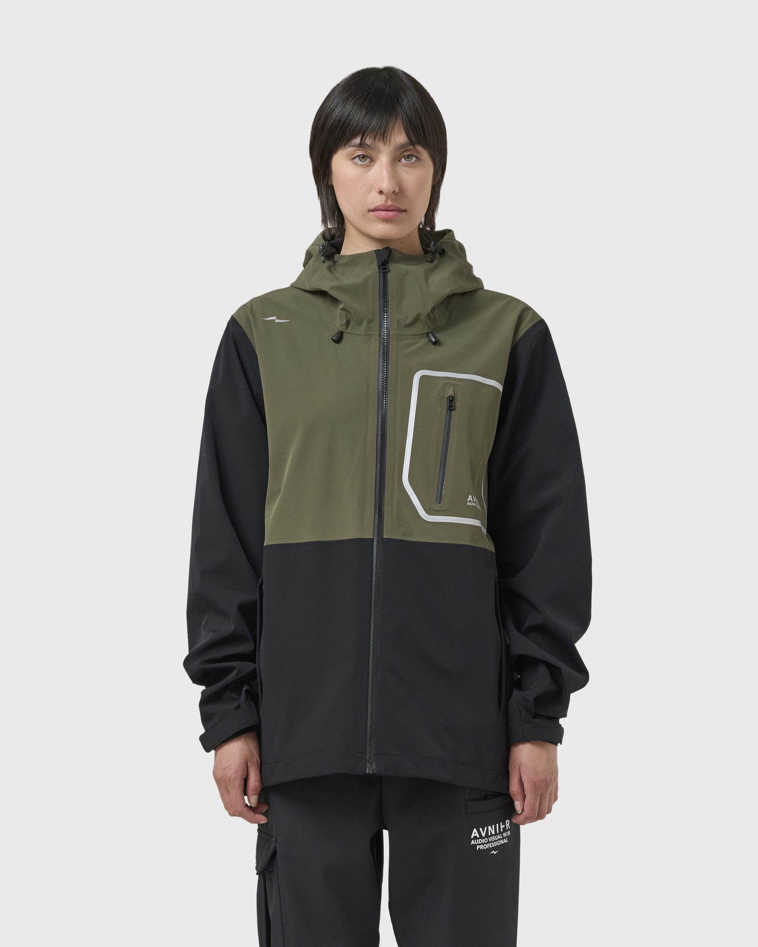 Veste Avnier Hardshell Interlude kaki portée par une femme, style workwear fonctionnel, coupe droite avec capuche réglable. - kaki