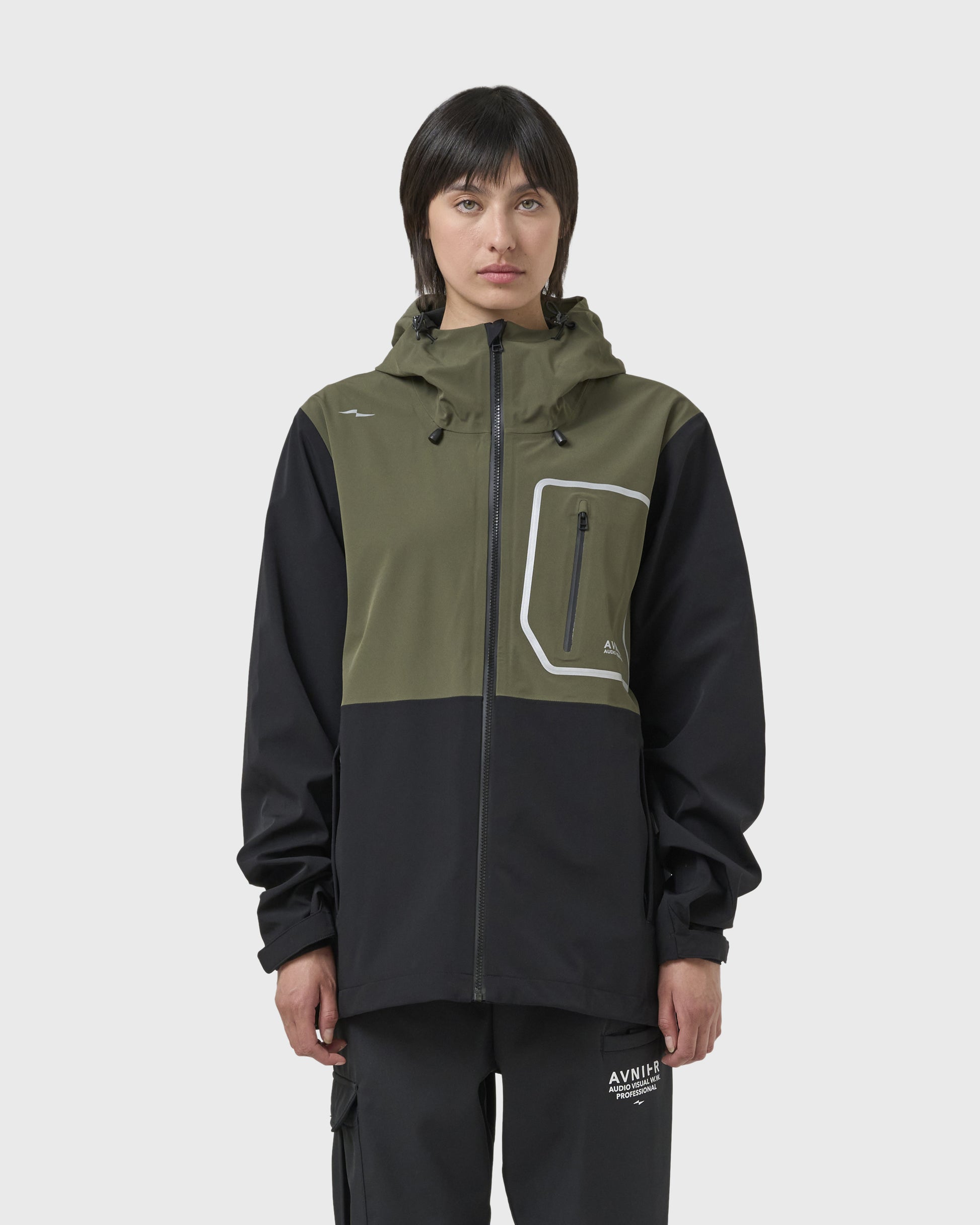 Veste Avnier Hardshell Interlude kaki portée par une femme, style workwear fonctionnel, coupe droite avec capuche réglable. - kaki
