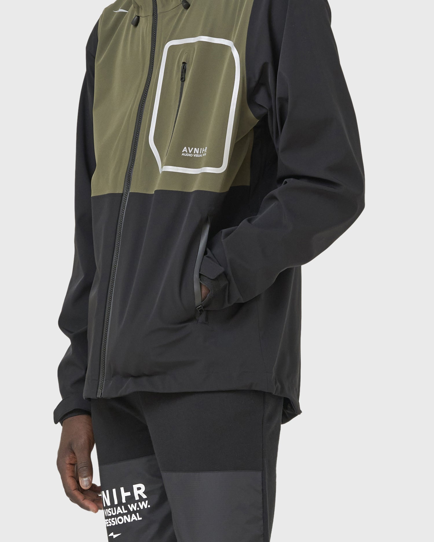 Profil de la veste Avnier Interlude kaki portée par un homme, matière coupe-vent et membrane respirante 3 couches. - kaki